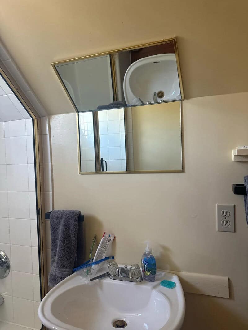 Bathroom mirror reflects sink and shower area, with towel hanging on wall.