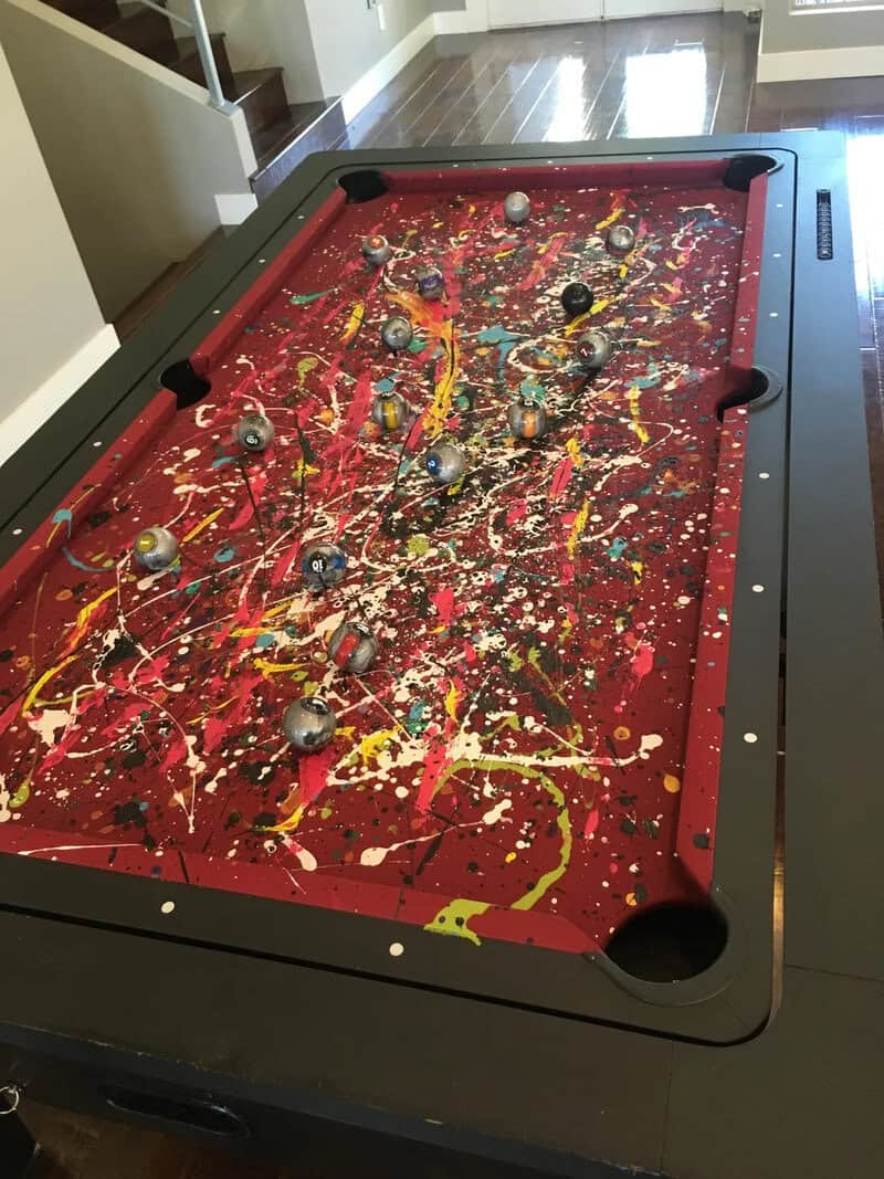 Messy pool table with scattered balls and colorful paint splatters.
