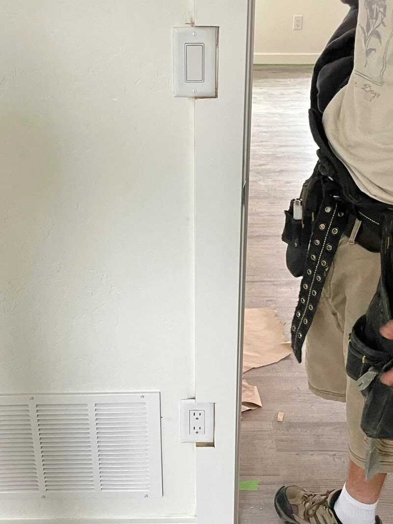 Partial view of a person in work attire standing near a wall with electrical outlets.