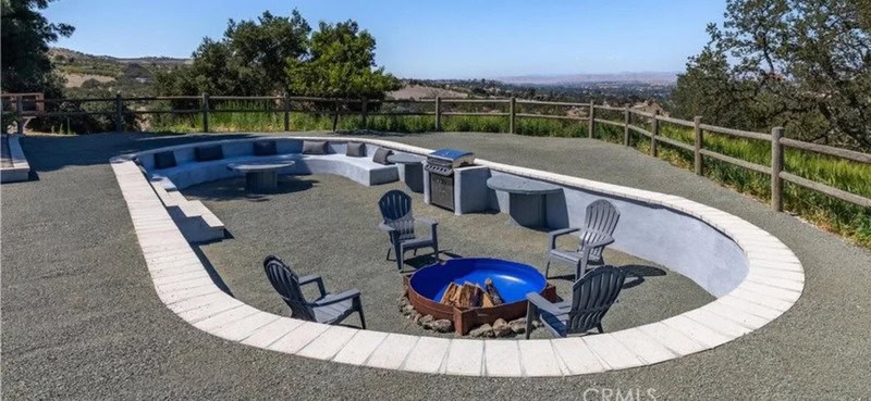 Empty backyard with a circular fire pit and chairs, overlooking a scenic landscape.