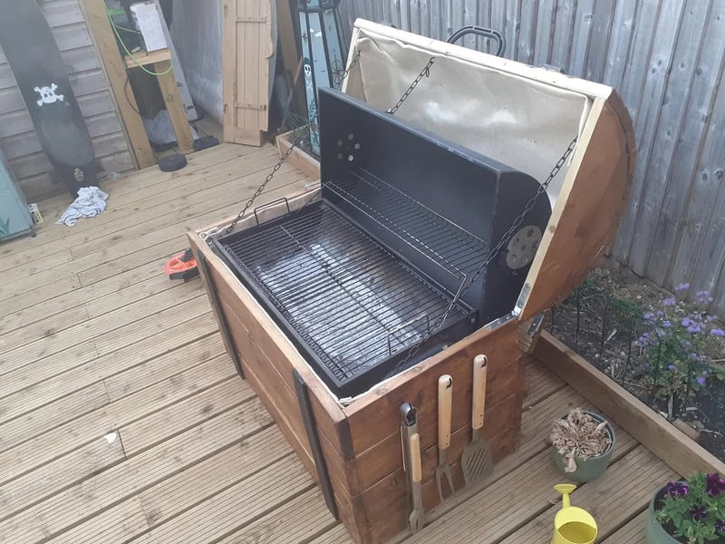 Barbecue grill built into a wooden outdoor storage box on a deck.