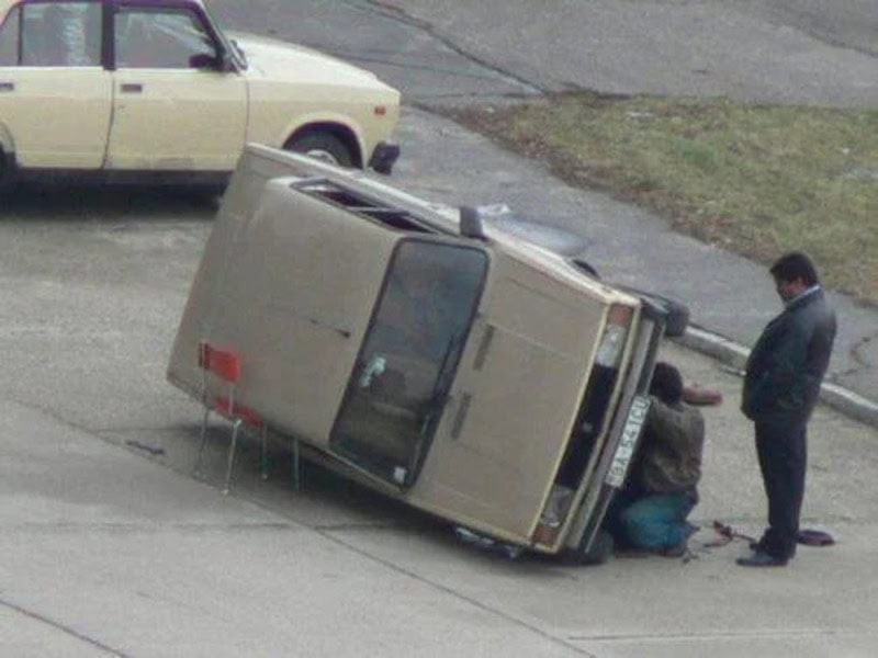 A van tipped over on its side with two men working on it, a man standing nearby.
