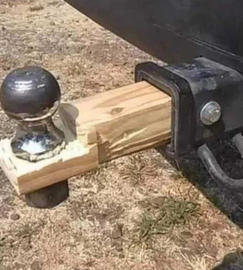 A trailer hitch with a wooden block and a metal ball on top, on dirt ground.