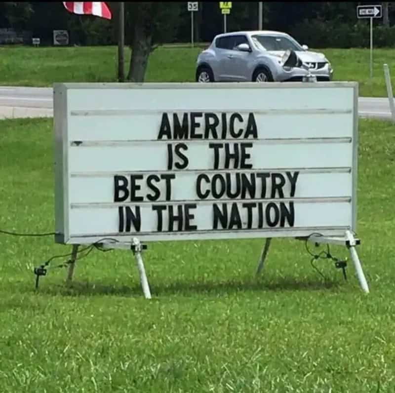 Sign reads 'America is the best country in the nation' with a car crash in the background.