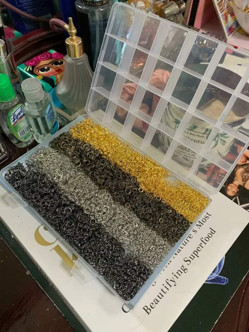 A plastic container with small metal rings in various colors, including silver, gold, and black.