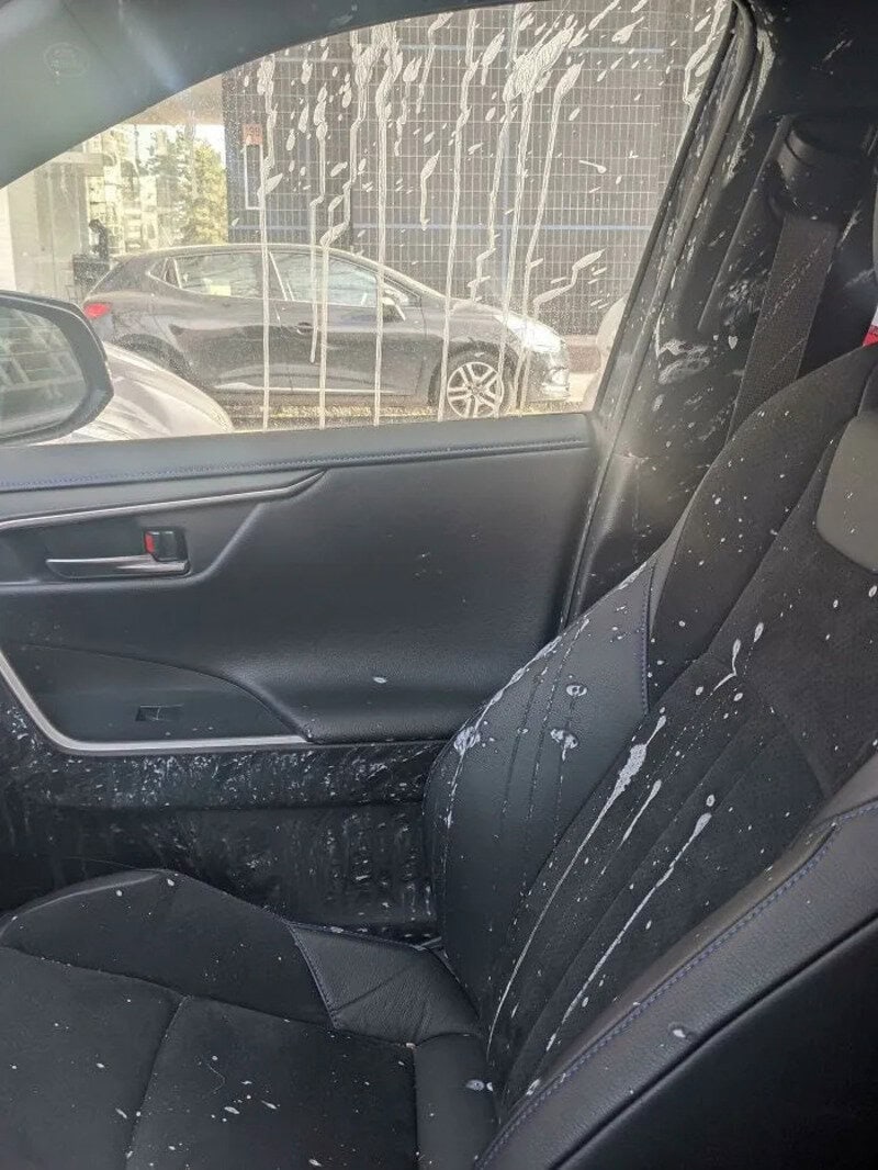 Car interior with soap suds on the seat and window, parked outside.