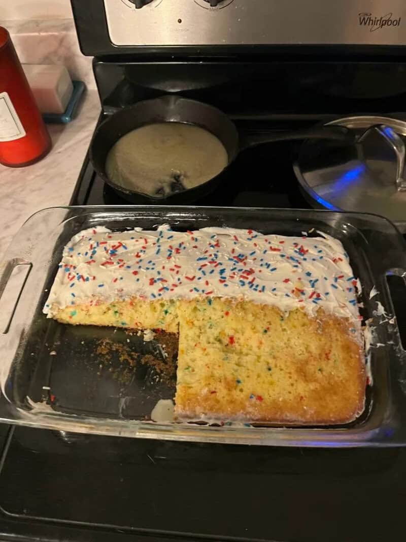 A partially eaten birthday cake with white frosting and colorful sprinkles on a glass dish.