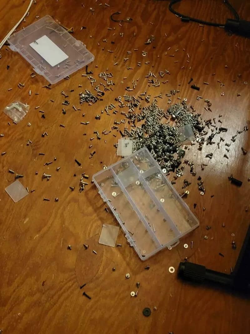 Disassembled electronic device with scattered screws and parts on a wooden surface.