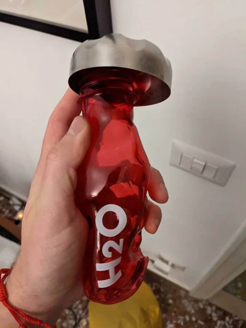 A hand holding a red, crumpled water bottle with a silver cap.