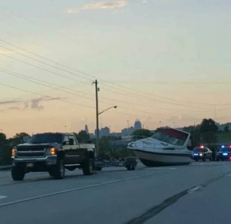 Boat on a trailer hitched to a pickup truck on the side of the road.