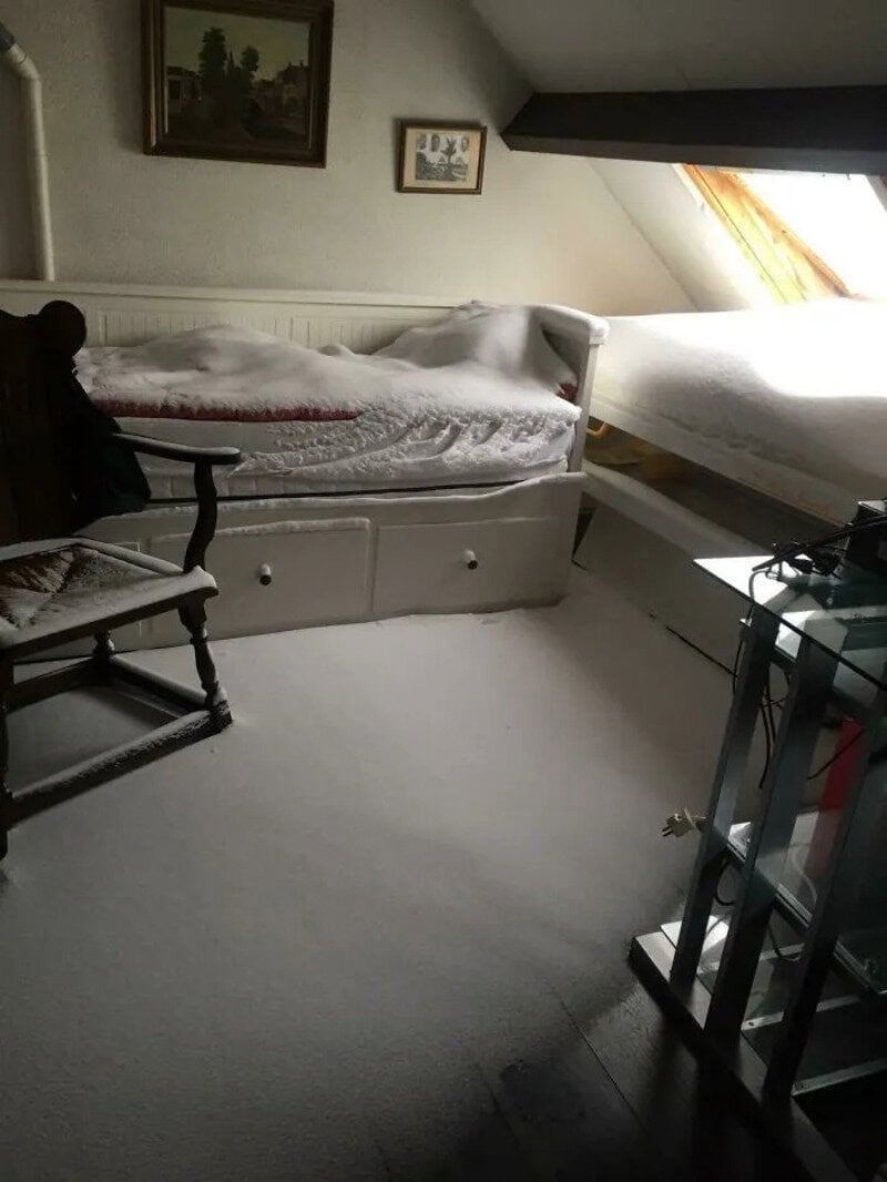 A bedroom with a bed under a sloped ceiling and a window, showing a messy setup.