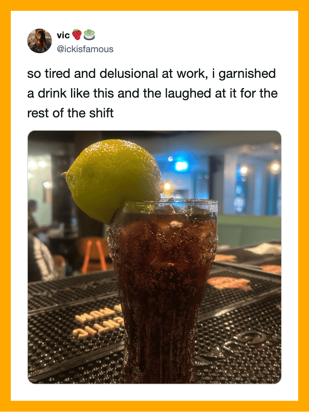 A glass of dark soda with a lemon wedge on the rim, on a bar counter.