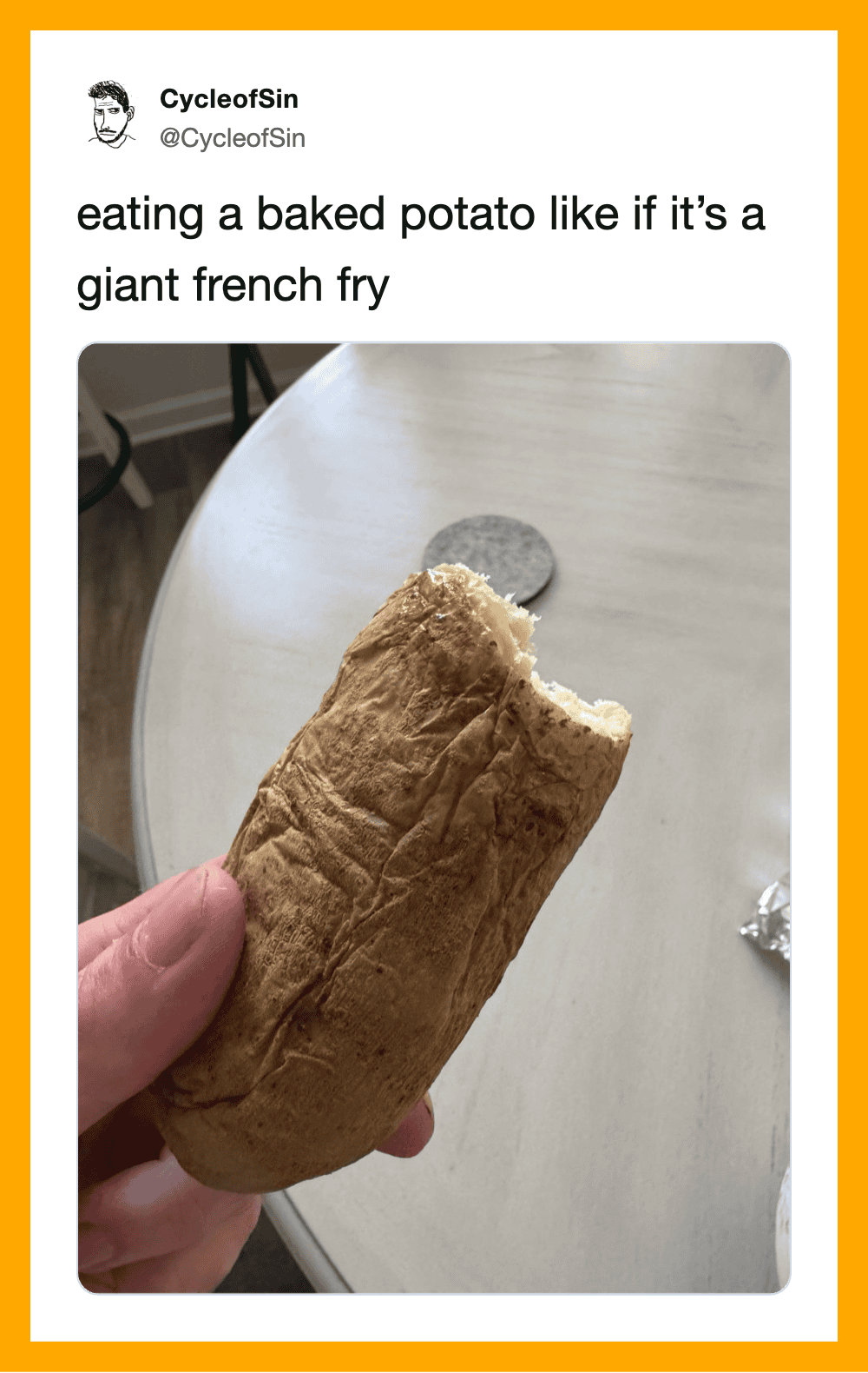Person holding a baked potato with a bite taken out, on a table.