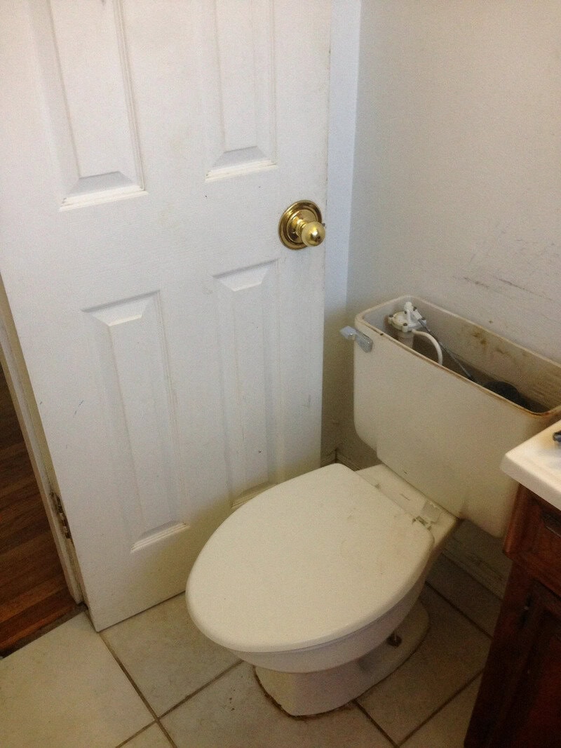 Toilet behind a door with a broken tank lid and a power strip on top.