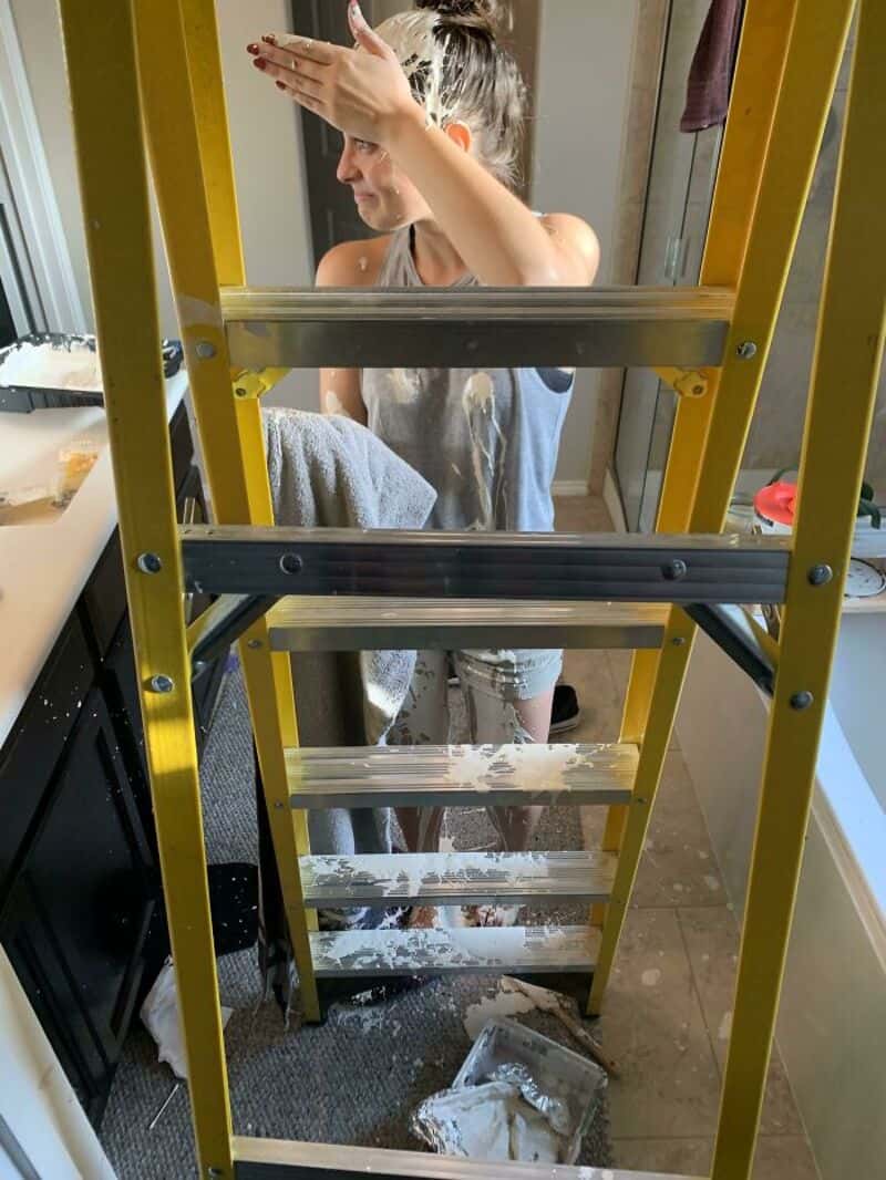 Woman cleaning window behind a yellow ladder in a kitchen.