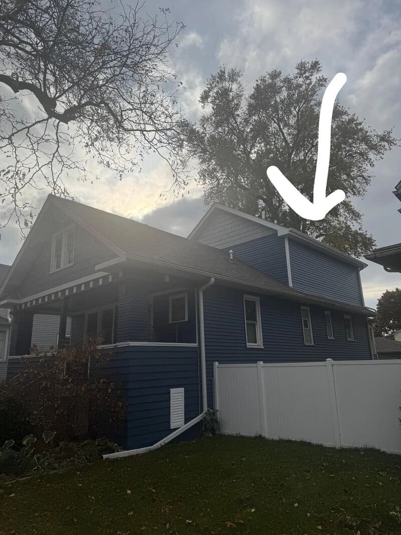 Blue house with a white fence and a large tree, with a white arrow pointing to the roof.