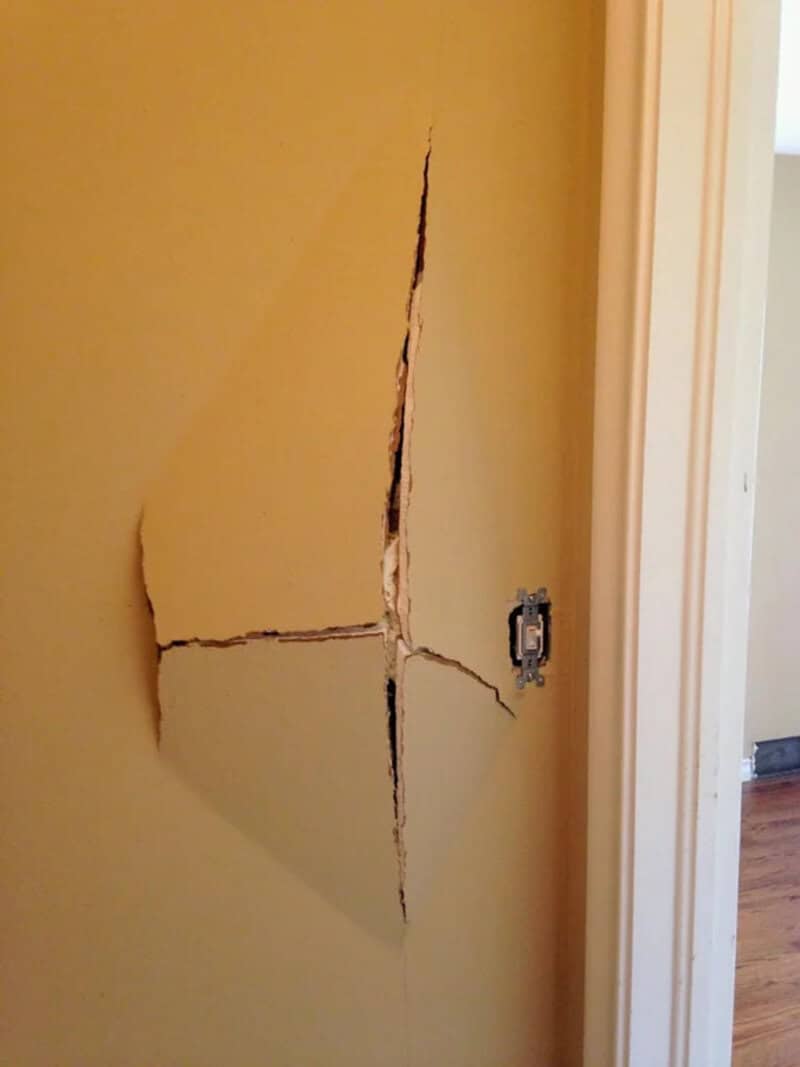 Large crack in yellow wall near door frame, with electrical outlet nearby.