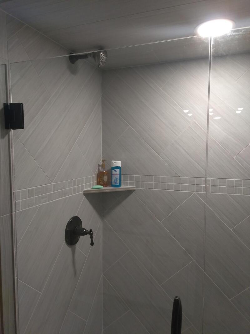 Shower with a shelf holding shampoo and soap, light fixture above, and a black faucet.