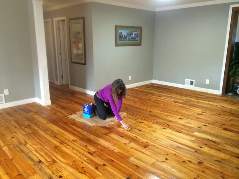 Woman cleaning a wooden floor in a spacious living room.