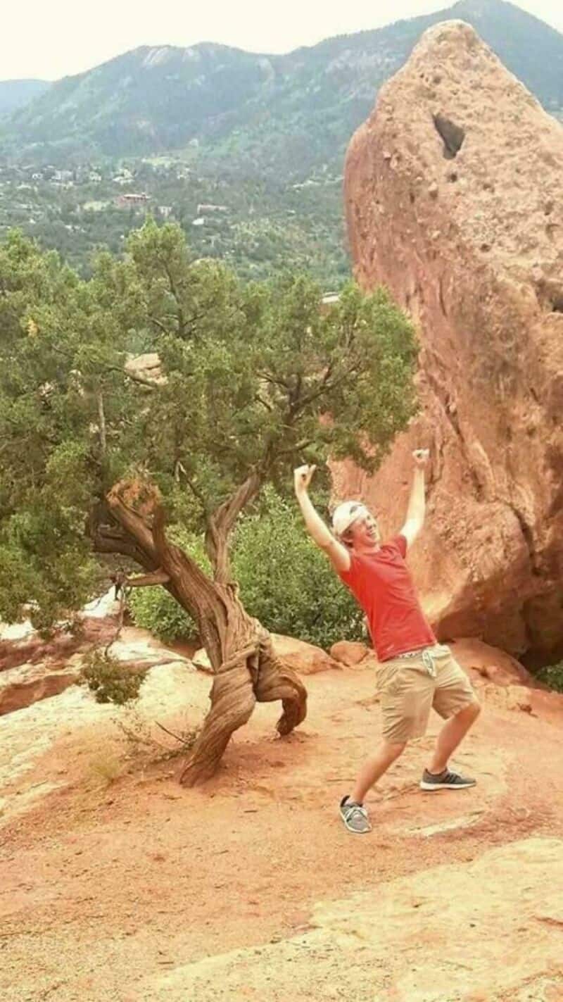 Person in red shirt and beige shorts pretending to hold a large boulder.