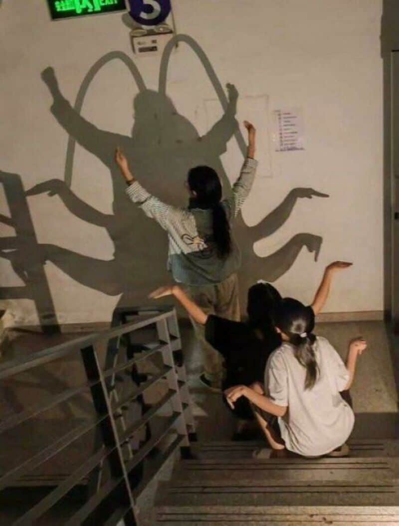 Girl and two children pose with shadow of a crab on the wall.