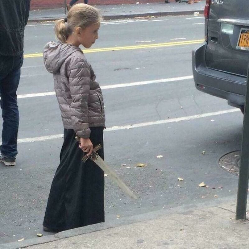 Girl holding a sword on the sidewalk near a parking meter.