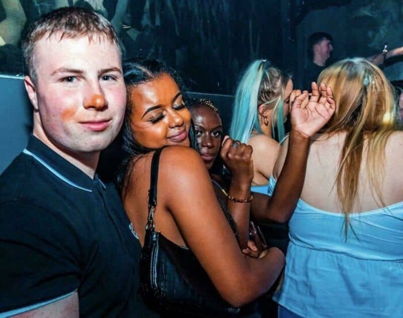 Group of young people at a party, some dancing and others posing for the camera.