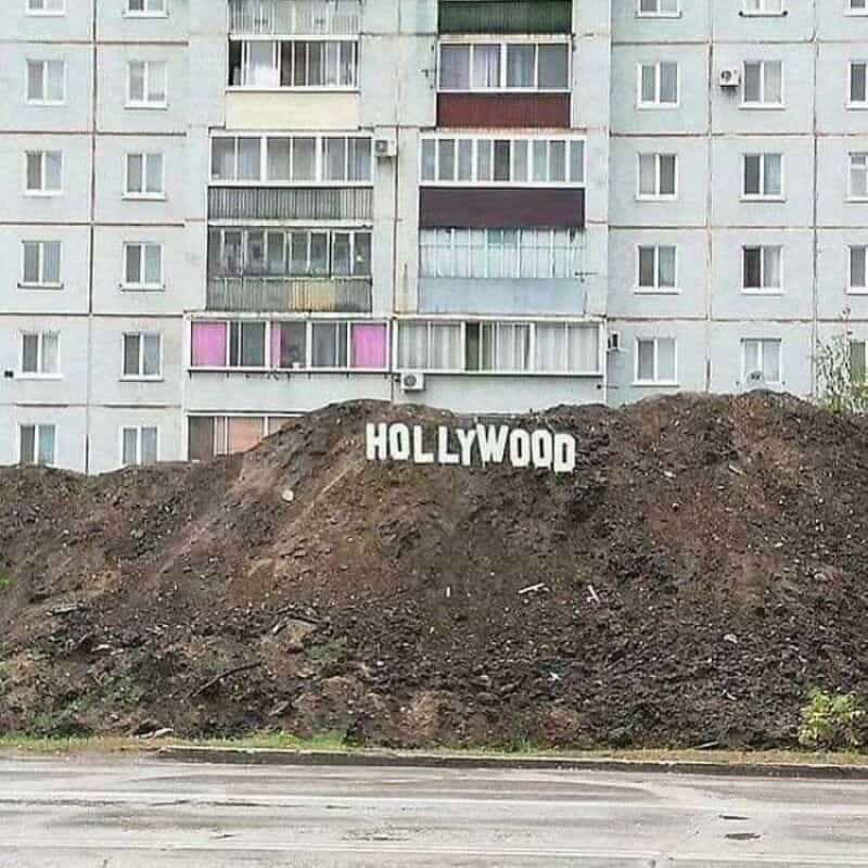 Hollywood sign placed on a dirt mound in front of an apartment building.