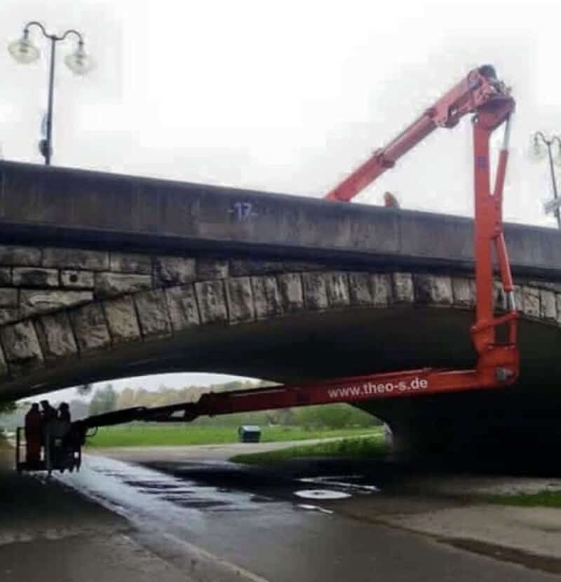Bridge repair using a large red crane under a stone bridge.
