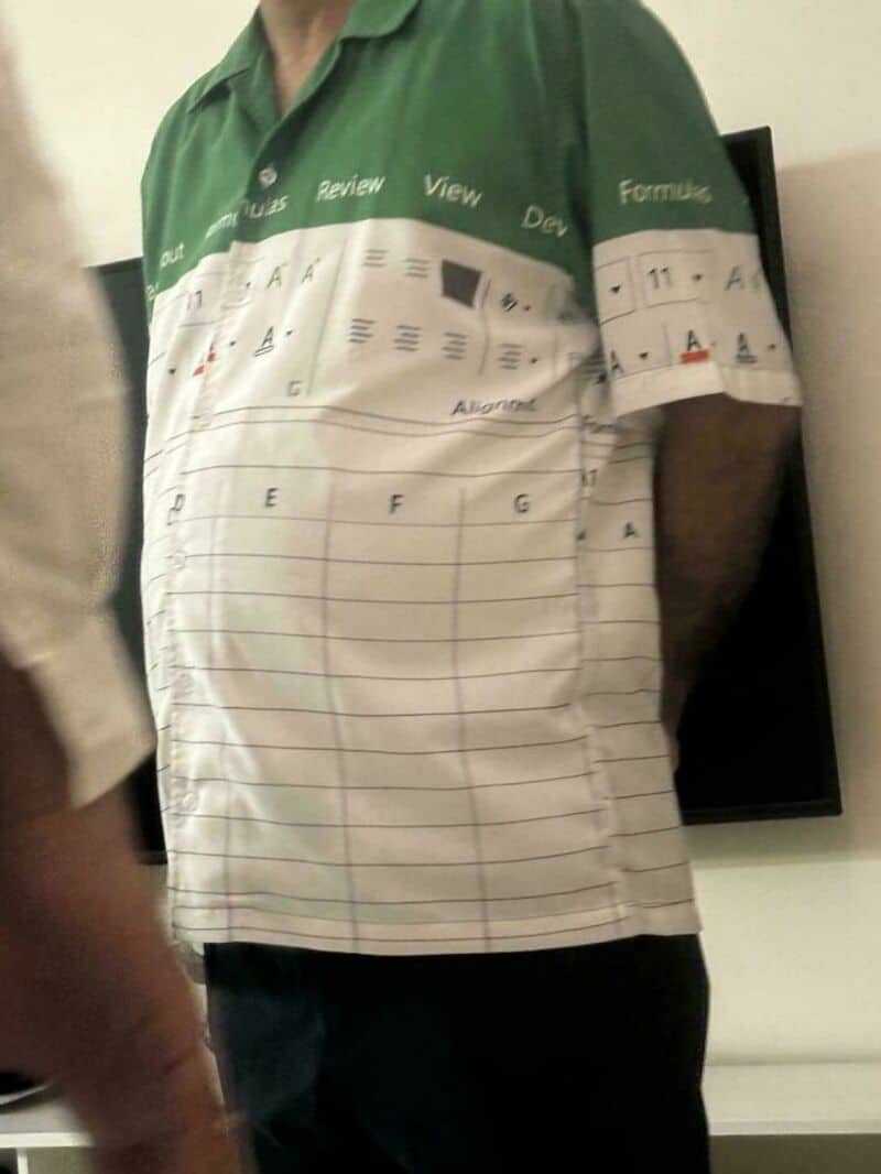 Person wearing a shirt with a printed spreadsheet design, standing indoors.