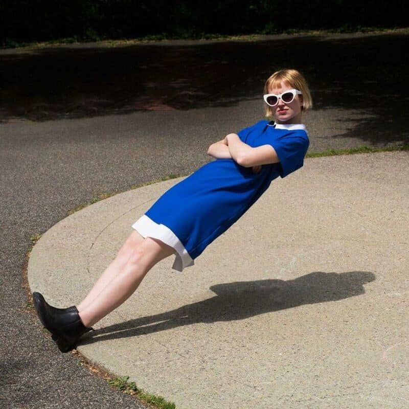 Girl in blue dress and sunglasses leaning back on a curved surface.