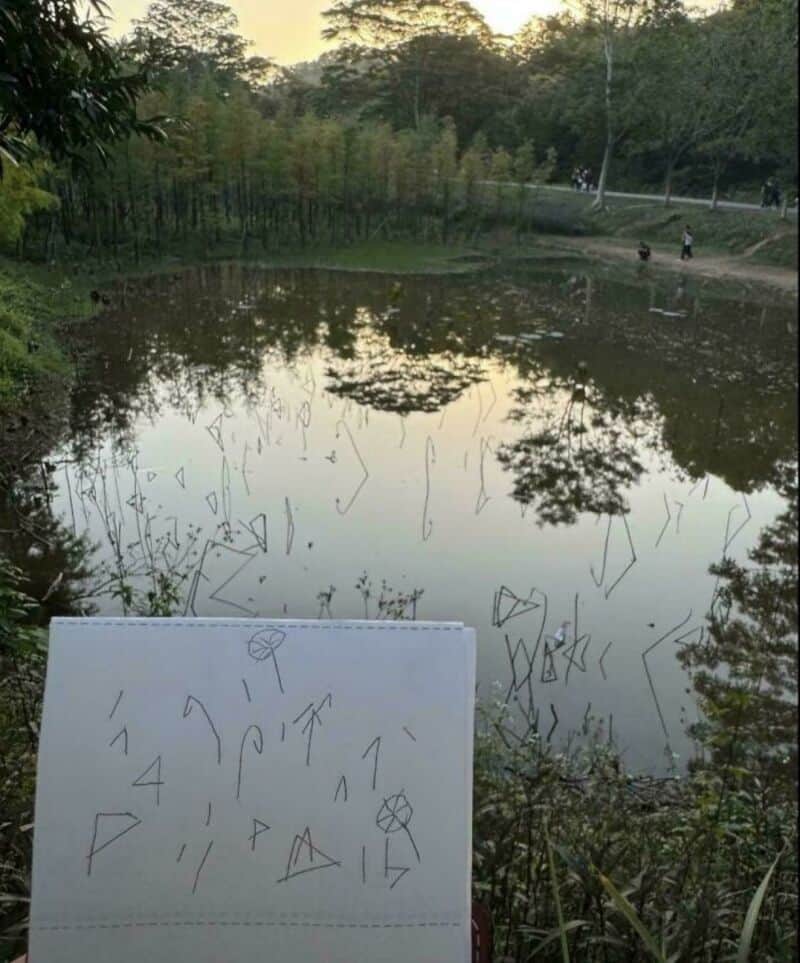 A pond with trees and people in the background, and a paper with geometric shapes in the foreground.