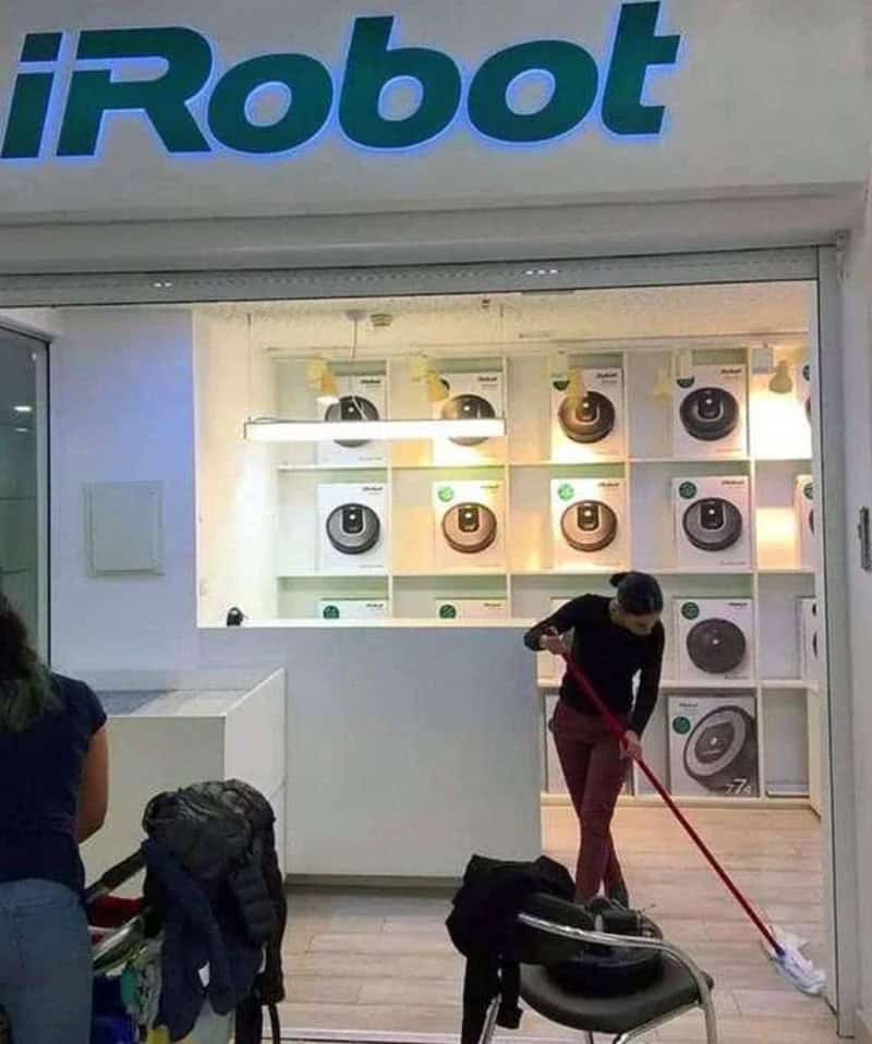 Person mops floor outside iRobot store with display of robot vacuums inside.