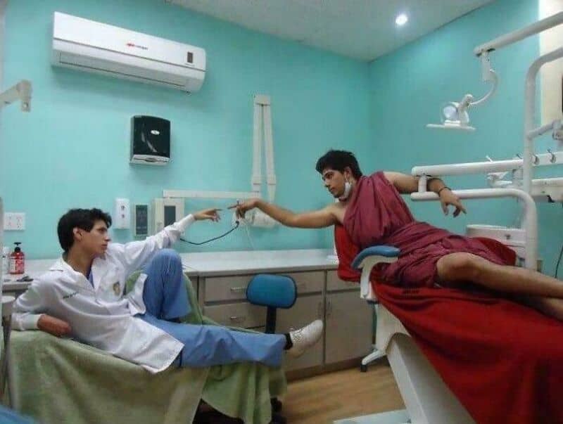 Two men in a hospital room, one lying on a bed and the other sitting, pointing at each other.