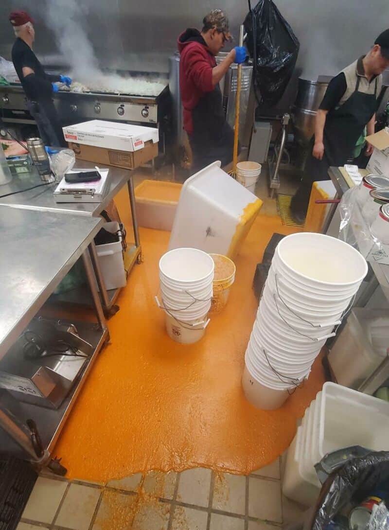 Kitchen with spilled orange liquid, buckets, and staff cleaning up mess.
