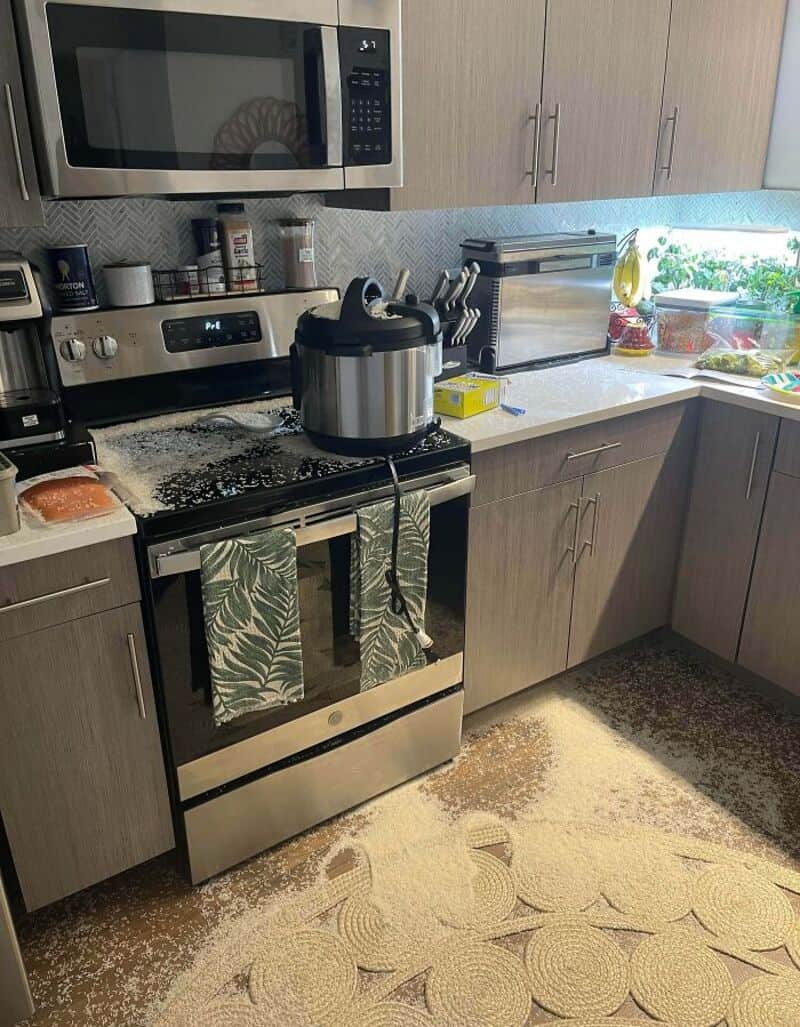 Messy kitchen with spilled rice on the floor and stove, microwave, and countertop cluttered.