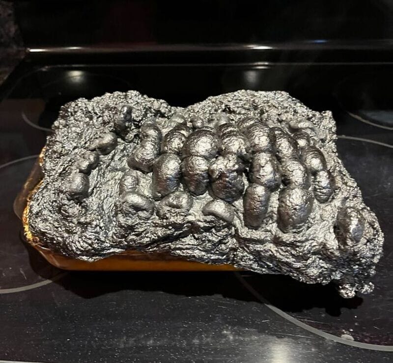 Charcoal-like object with metallic, bumpy surface on a black stovetop.