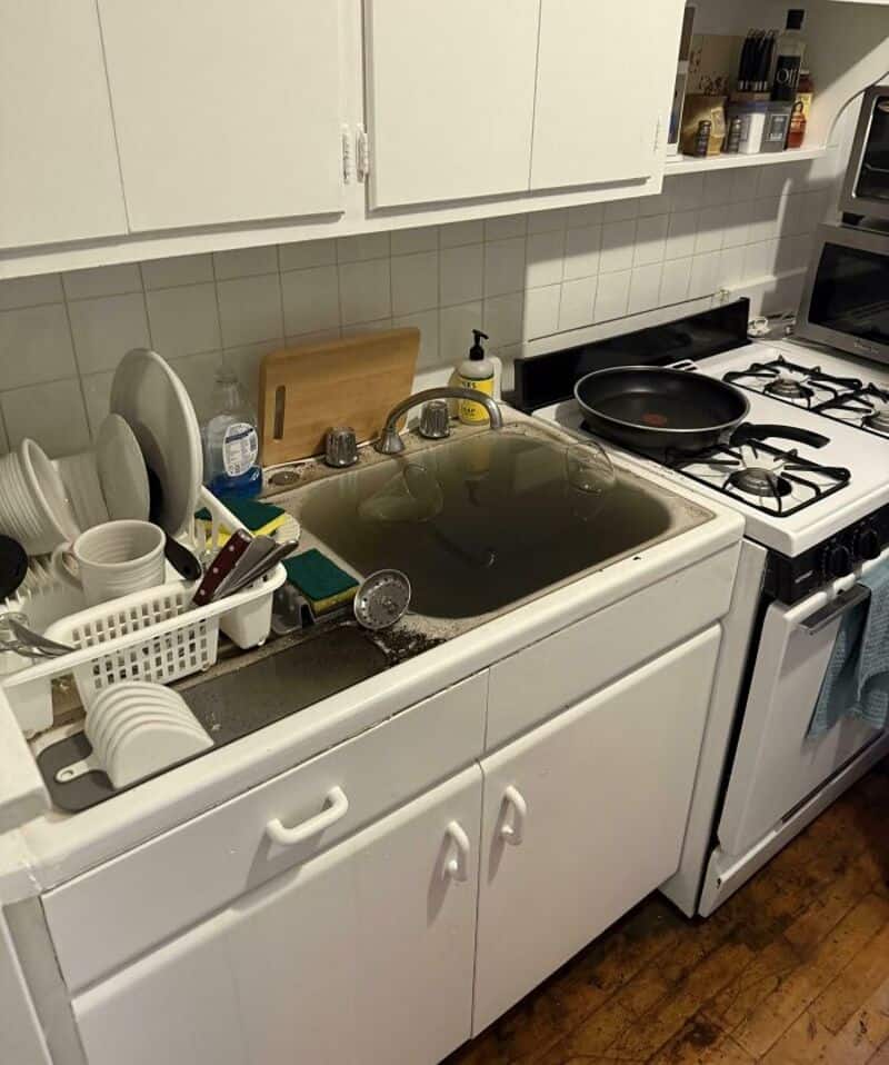 Burnt pan on stove in a cluttered kitchen with dishes and utensils.