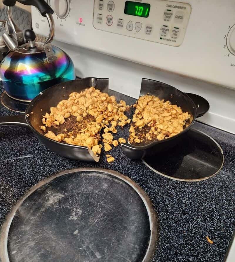 Split frying pan with scrambled eggs spilling out onto stove.