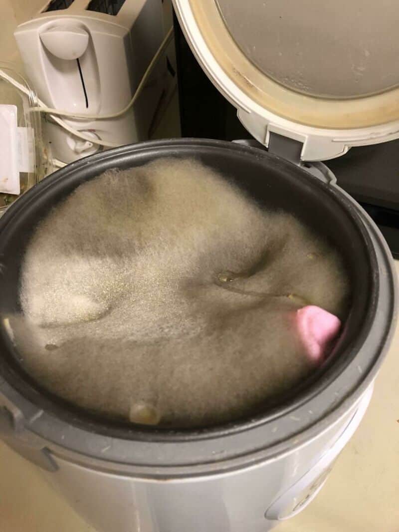 A washing machine filled with dirty, soapy water and a pink object inside.