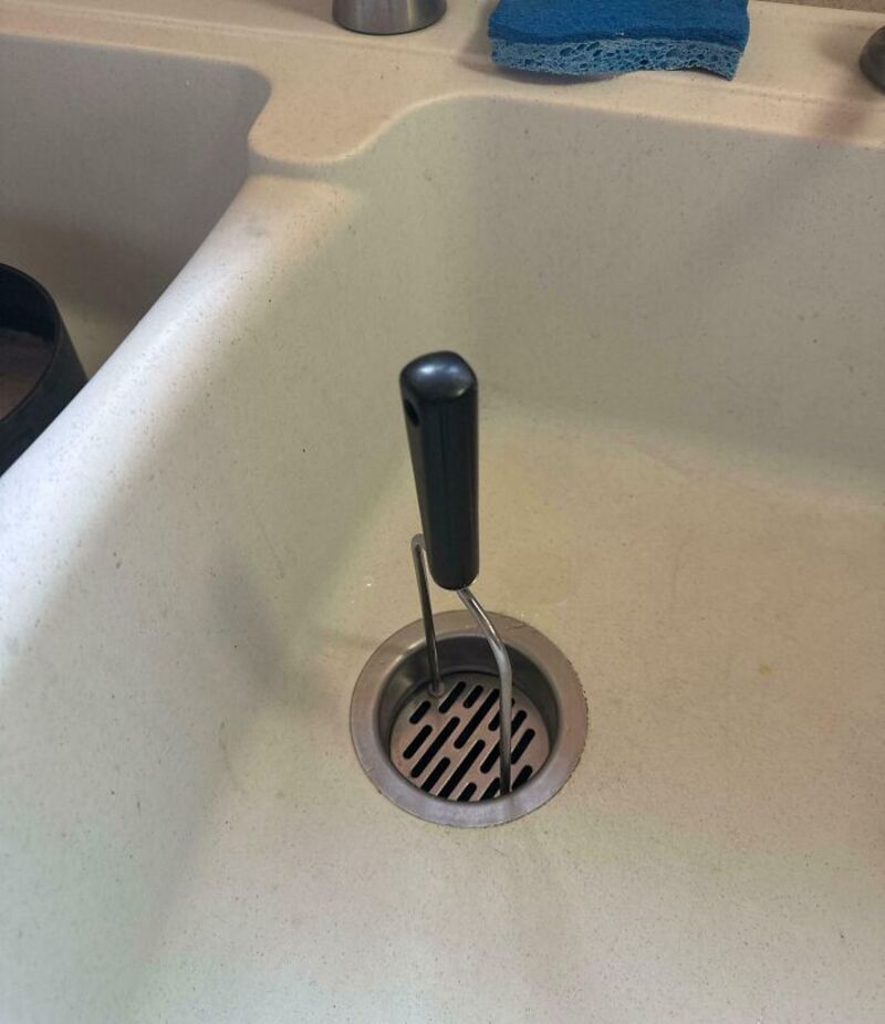 Kitchen sink with a black-handled utensil stuck in the drain.