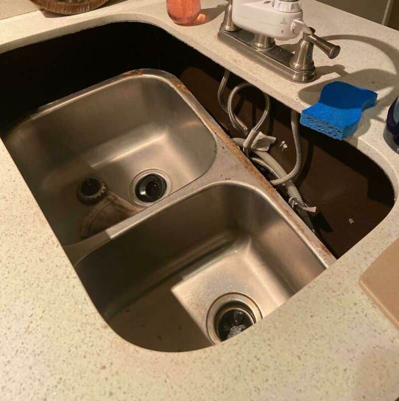 Kitchen sink with rust and grime around the edges, missing faucet, and cluttered countertop.