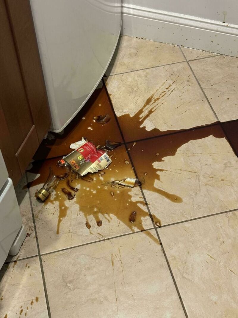 Spilled coffee and broken mug on kitchen floor near fridge and wall.