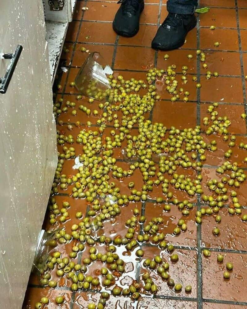Spilled green peas on a tiled kitchen floor with a person's feet nearby.