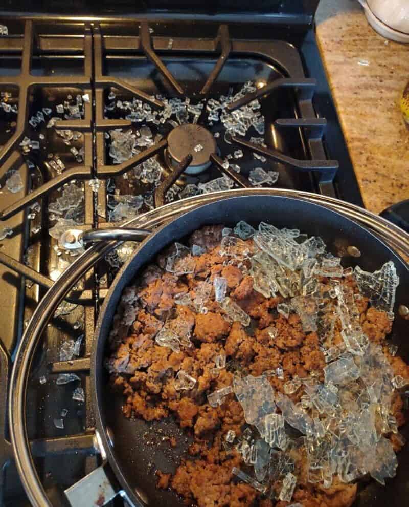 Broken glass on a stove with a frying pan of cooked ground meat.