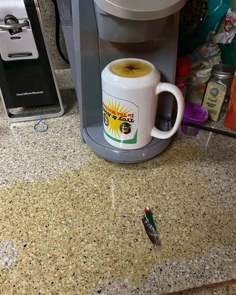 Coffee mug with burnt coffee on top, on a kitchen counter with a knife nearby.