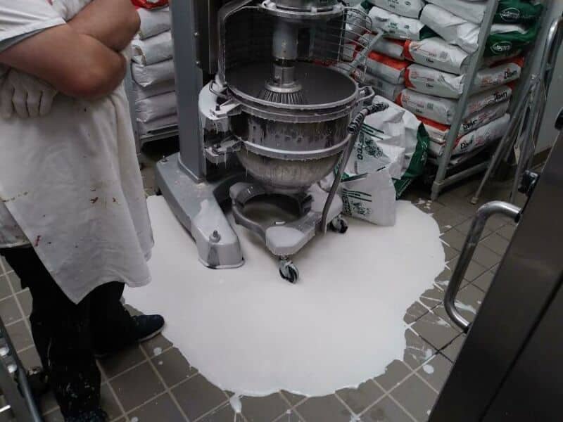 A large amount of spilled white liquid on the floor around a commercial mixer in a kitchen.