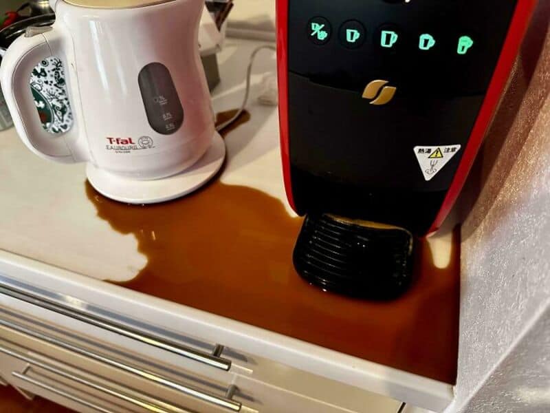 Coffee machine with spilled coffee on the counter in front of a black and red appliance.