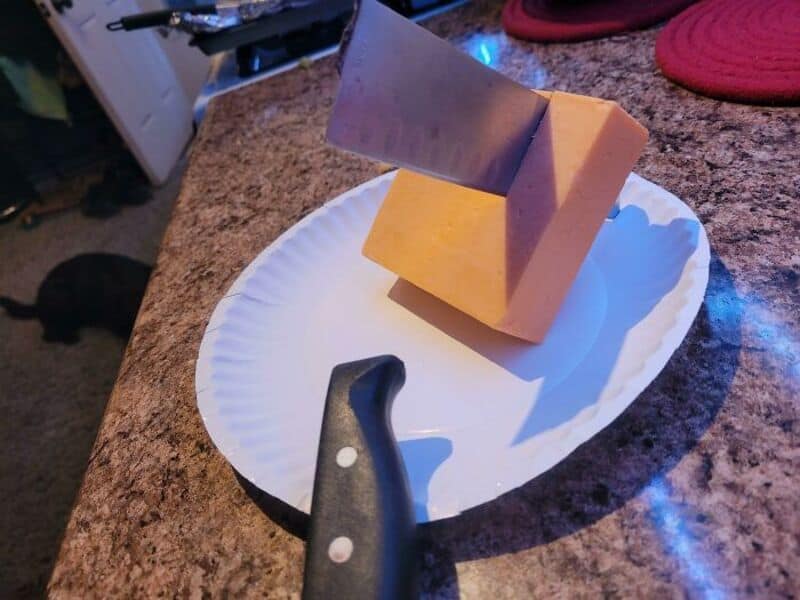 Cheese block with a large knife stuck in it on a paper plate.