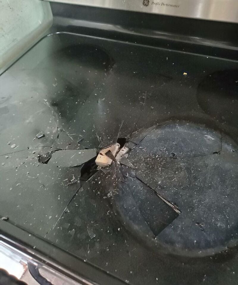 Broken glass on a black stovetop with a large crack and shattered pieces.